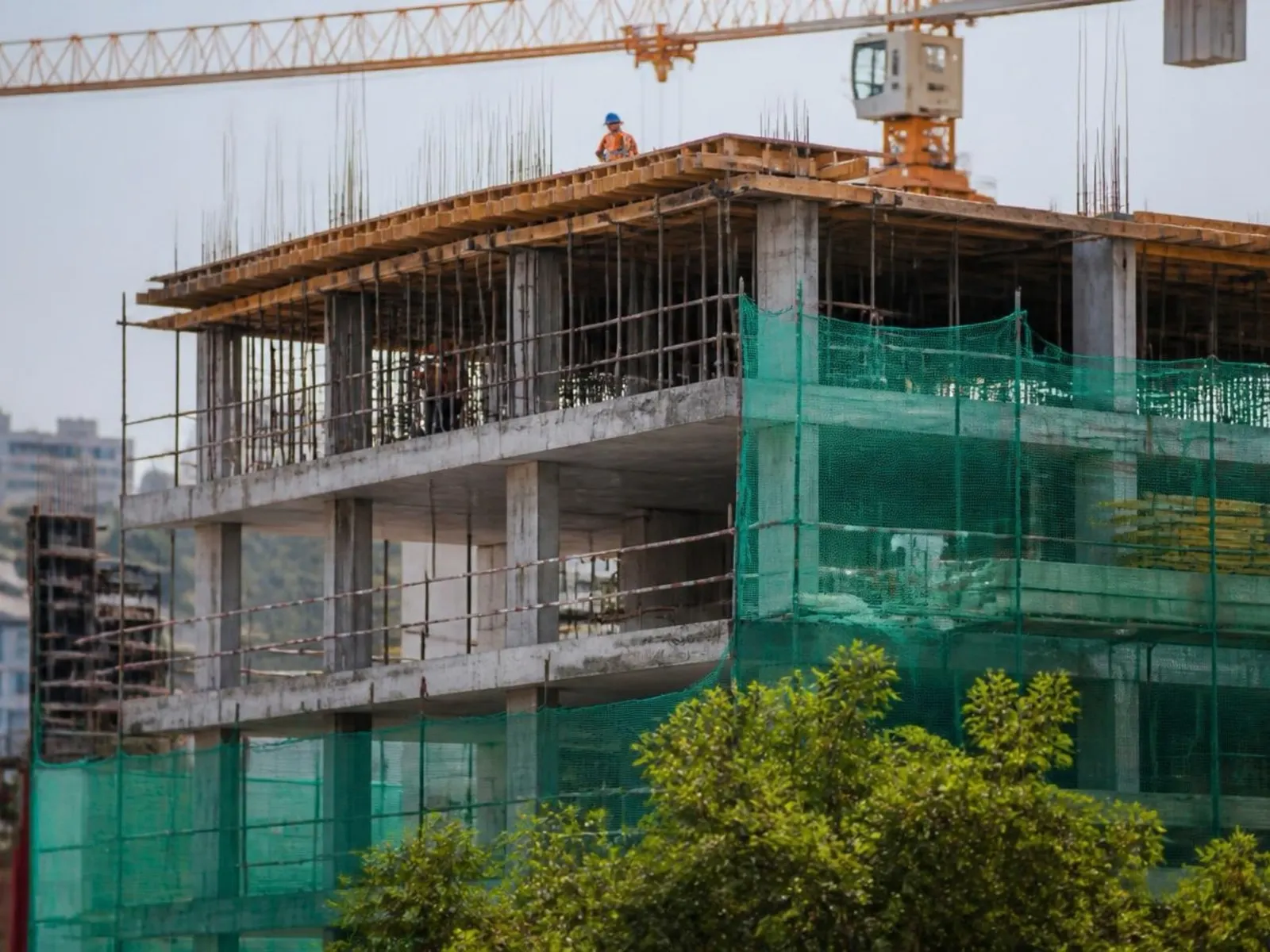 Yıkımı tamamlanmış parselde temel kazısı: ekskavatör çalışıyor, arkada eski apartmanların cephesi duruyor.